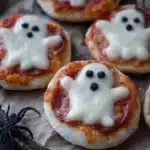 Spooktacular mini ghost pizzas on a baking tray, ready for Halloween celebrations.