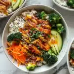 Sticky chicken rice bowls garnished with fresh vegetables and sauce.
